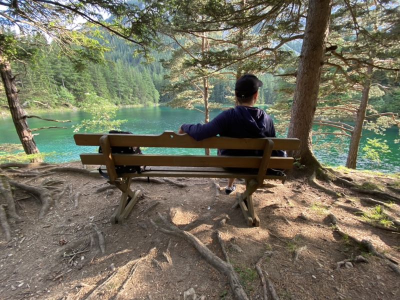 Človek oddychuje na lavičke a sleduje smaragdové vody jazera Grüner See