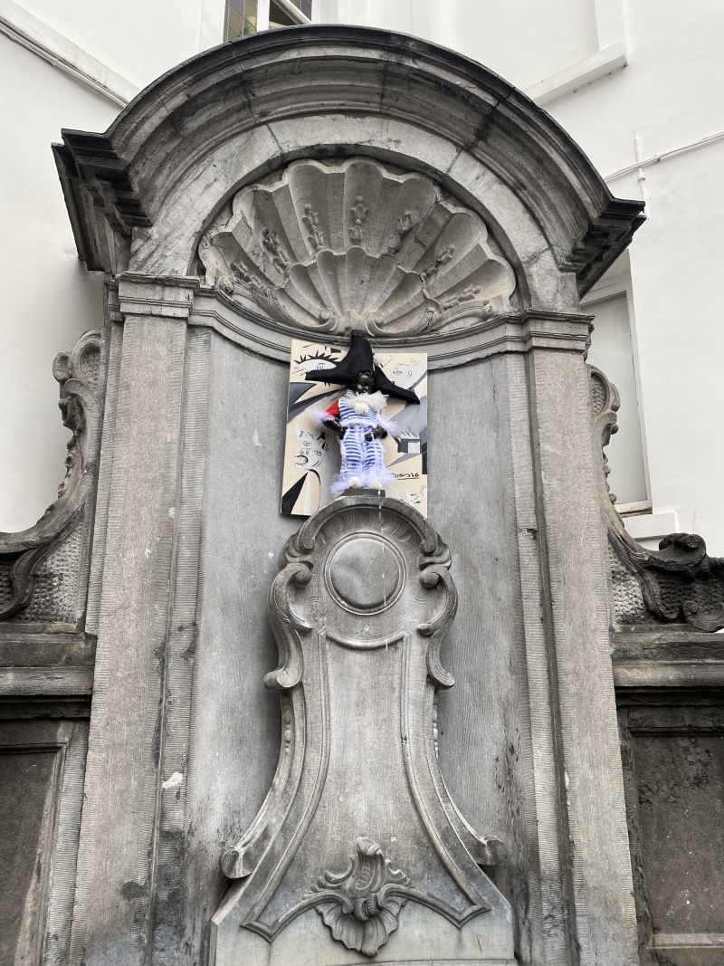 čo vedieť pred cestou do Bruselu - kamenná fontána Manneken Pis s bronzovou sochou cikajúceho chlapca, ktorý ma na hlave trojrohý klobúk a má oblčený pruhovaný modrobiely kostým