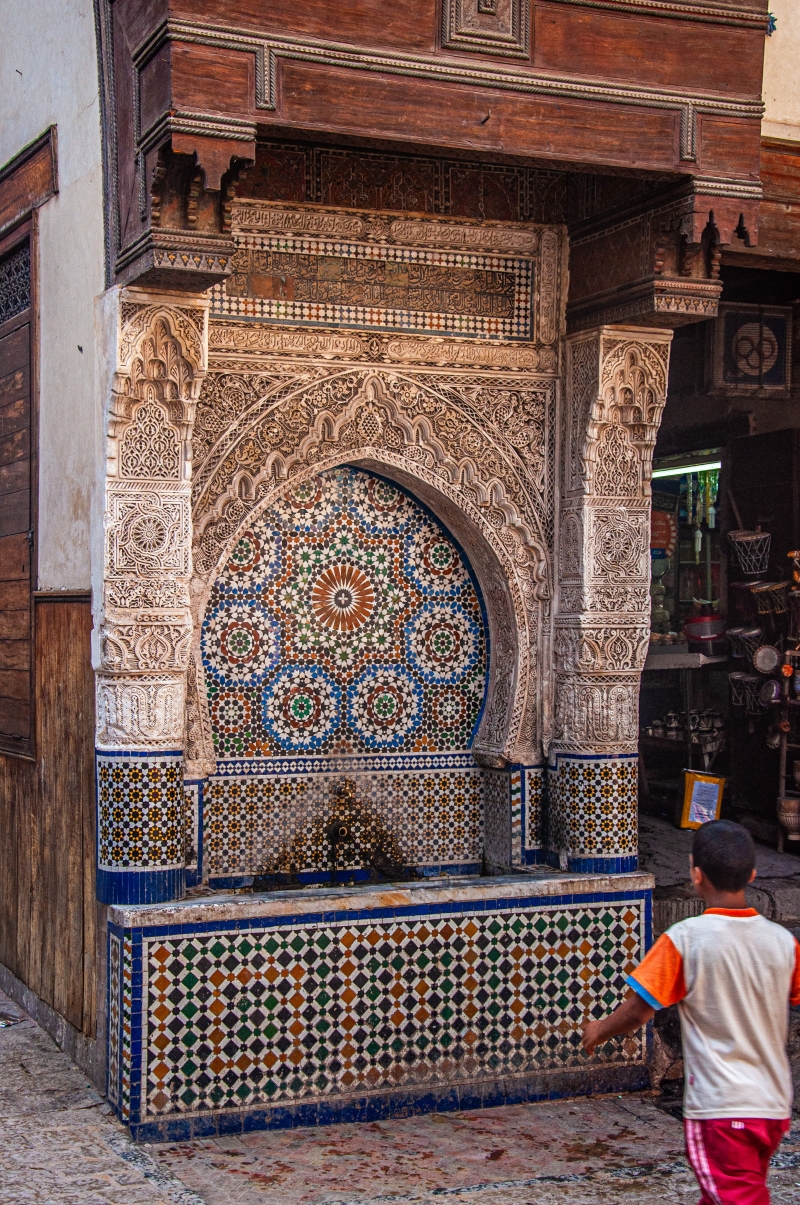 Fés, medina - malý chlapec beží k fontáne nádherne zdobenej islamskými vzormi
