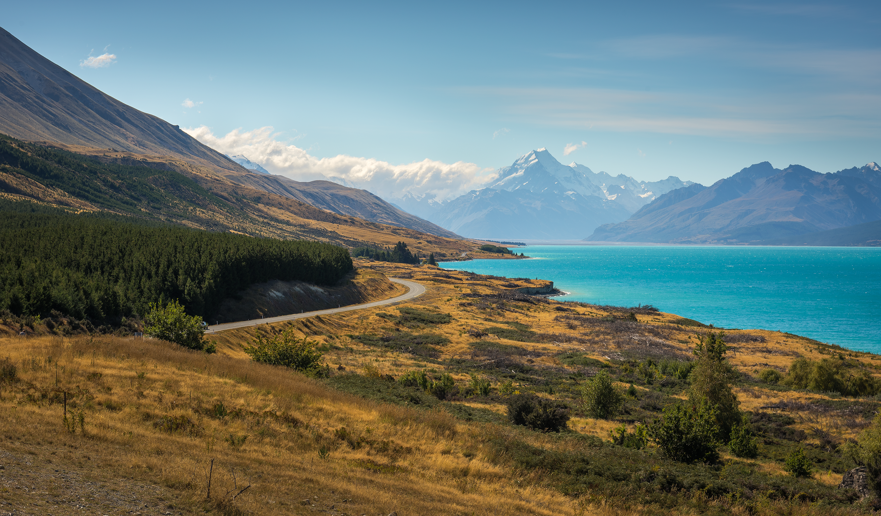 čo vidieť na Novom Zéland - Južný ostrov: na pravej strane tyrkysové vody jazera Pukaki, vľavo cesta k vrchom Národného parku Mount Cook, ktoré sú v pozadí